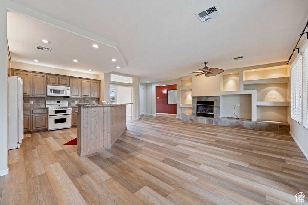 Kitchen with white appliances, light wood-style flooring, a tiled fireplace, recessed lighting, and a center island