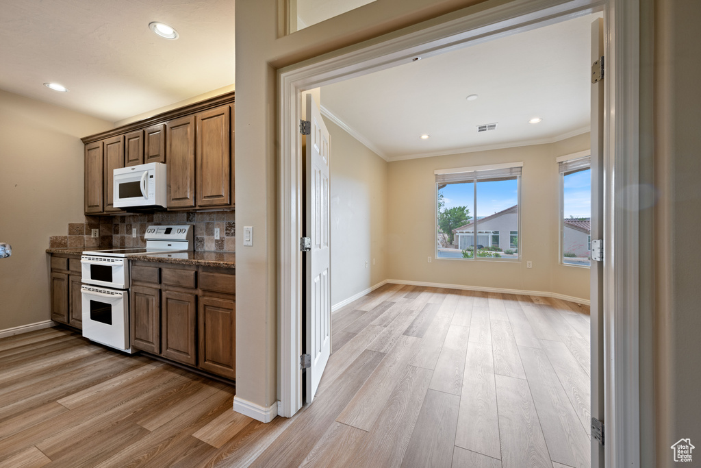 Kitchen with white appliances, crown molding, light wood-type flooring, backsplash, and recessed lighting