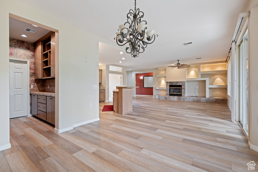 Unfurnished living room featuring light wood finished floors, ceiling fan, a tile fireplace, recessed lighting, and a chandelier