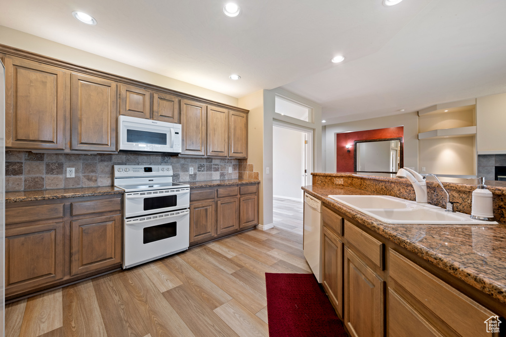 Kitchen with white appliances, light wood-type flooring, decorative backsplash, recessed lighting, and dark stone countertops