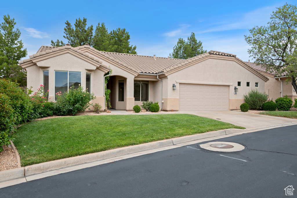View of front facade with a garage, a front lawn, a tiled roof, stucco siding, and concrete driveway