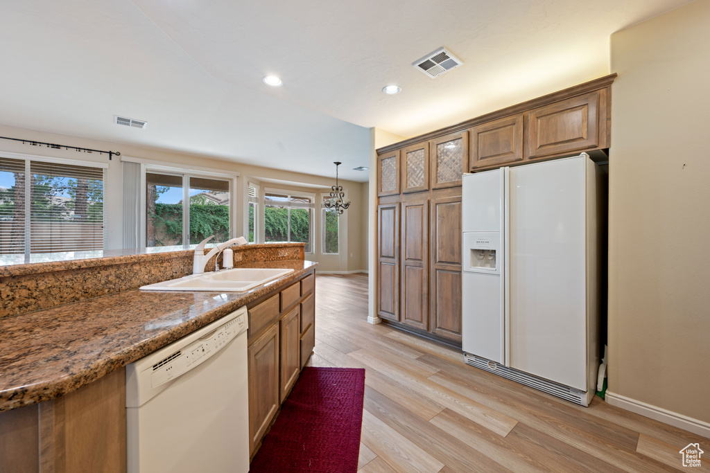 Kitchen featuring white appliances, light wood-style flooring, brown cabinets, a chandelier, and recessed lighting