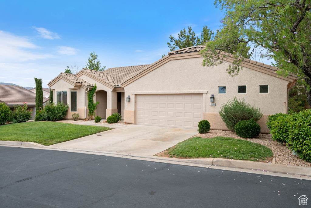 Mediterranean / spanish-style house with an attached garage, a tile roof, stucco siding, and concrete driveway