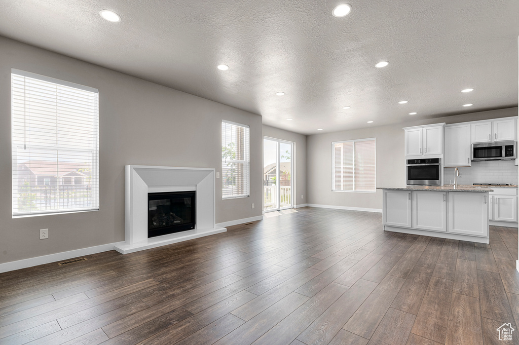 Unfurnished living room featuring a textured ceiling, dark wood finished floors, recessed lighting, and a glass covered fireplace