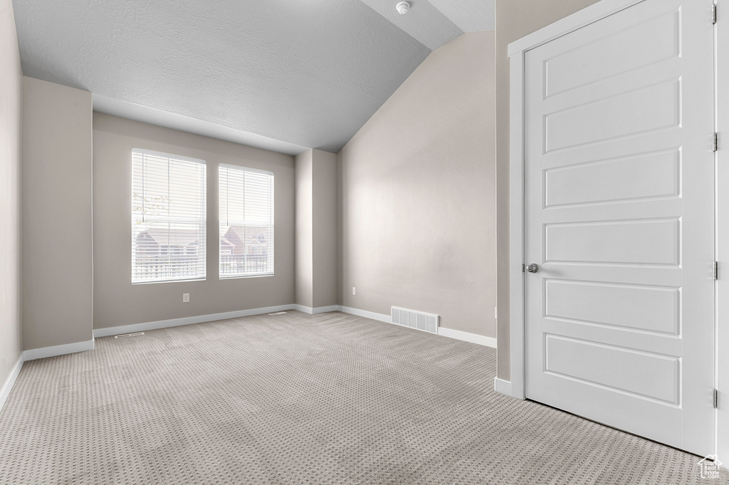 Carpeted spare room with vaulted ceiling and a textured ceiling