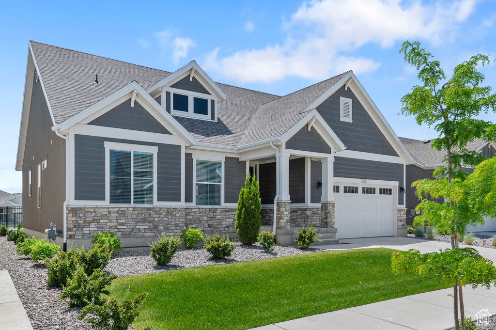 Craftsman house featuring stone siding, a front lawn, a garage, and concrete driveway