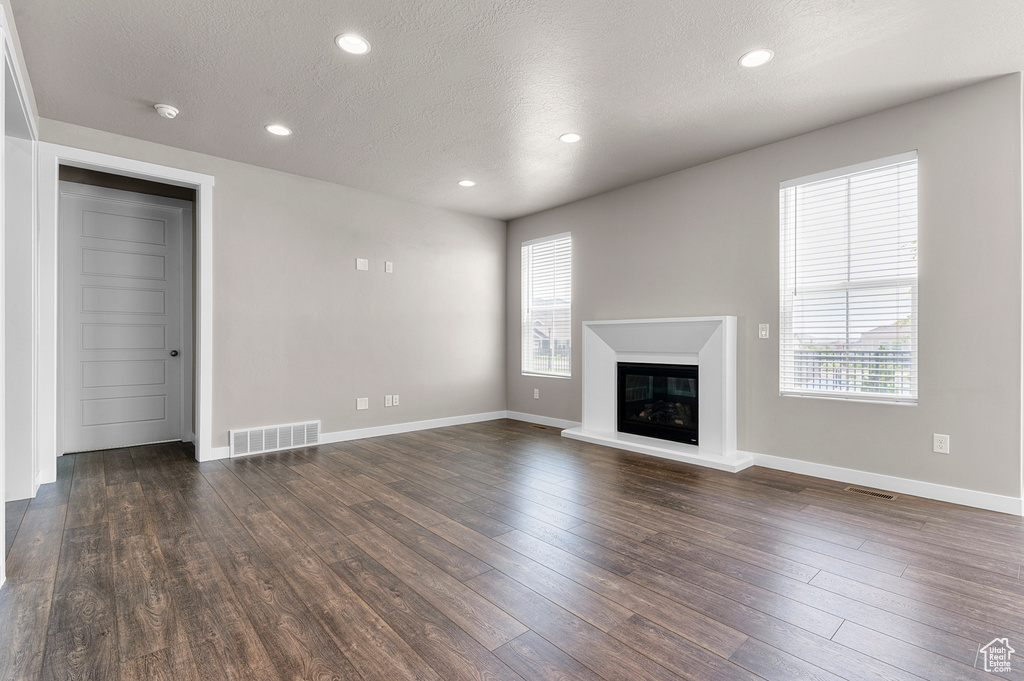 Unfurnished living room featuring healthy amount of natural light, dark wood-type flooring, a glass covered fireplace, recessed lighting, and a textured ceiling