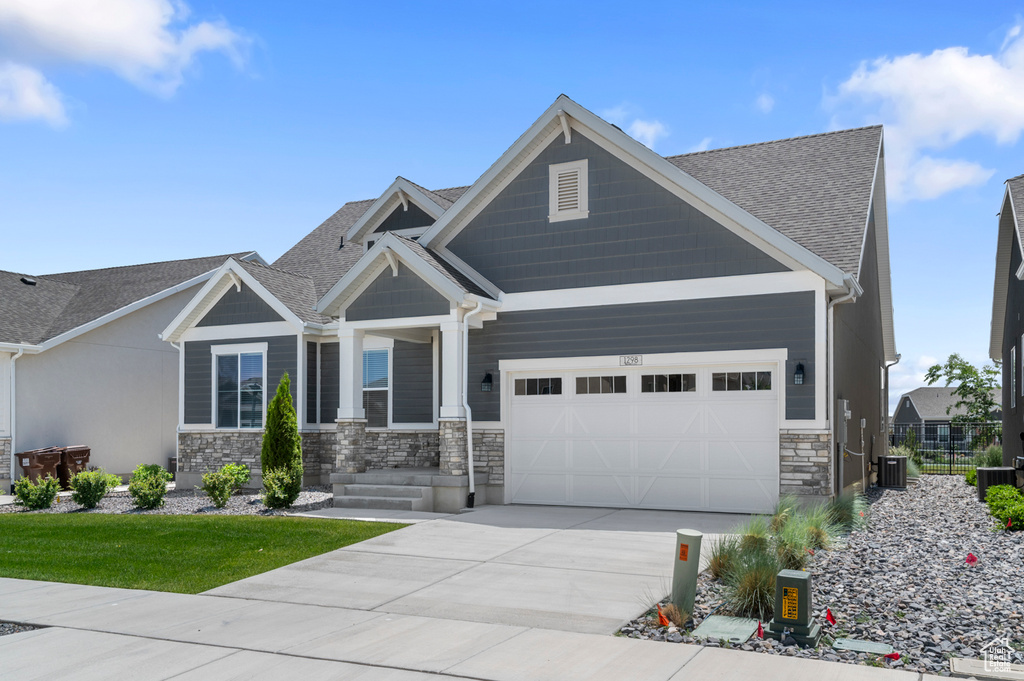 Craftsman-style house featuring a garage, stone siding, concrete driveway, and a shingled roof