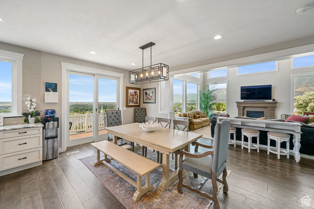 Dining room with dark wood-type flooring, recessed lighting, a fireplace, and a chandelier