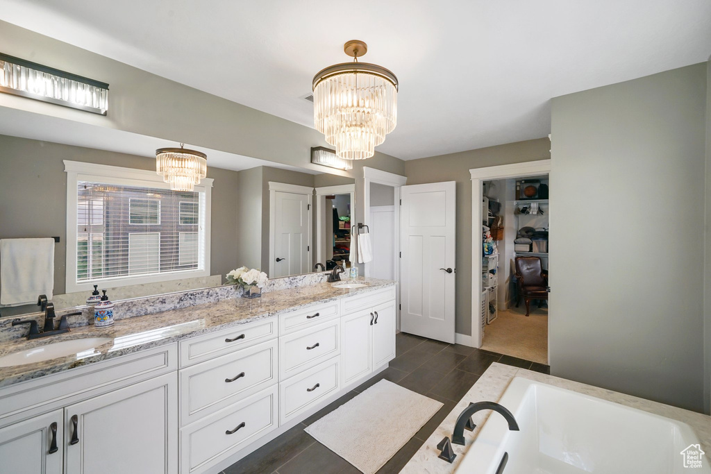 Full bath with double vanity, a chandelier, a spacious closet, a bathtub, and wood finished floors