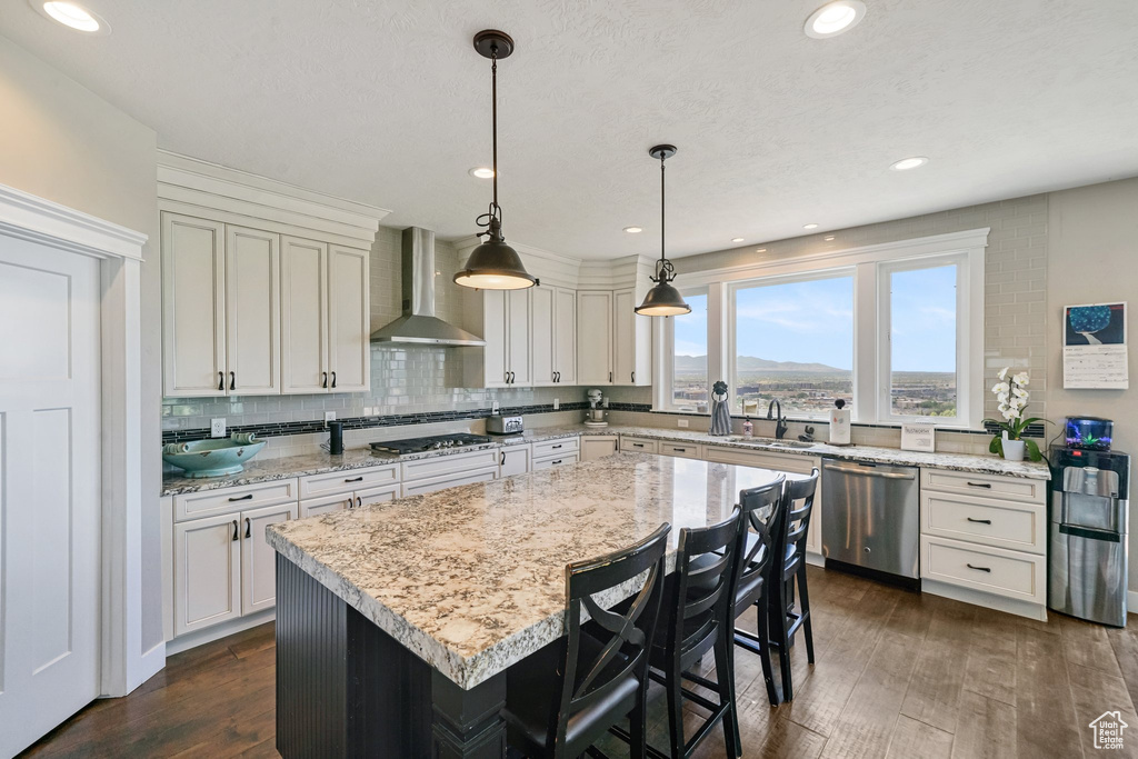 Kitchen with wall chimney range hood, stainless steel appliances, dark wood-style floors, backsplash, and a kitchen island