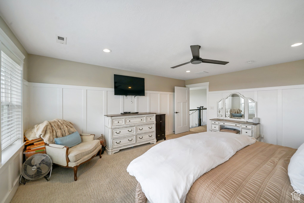 Bedroom with a decorative wall, light colored carpet, ceiling fan, wainscoting, and recessed lighting