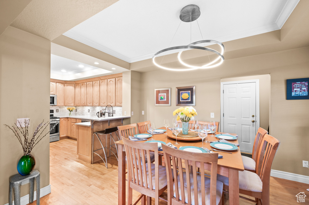 Dining area featuring a tray ceiling, crown molding, light wood-style floors, a chandelier, and recessed lighting