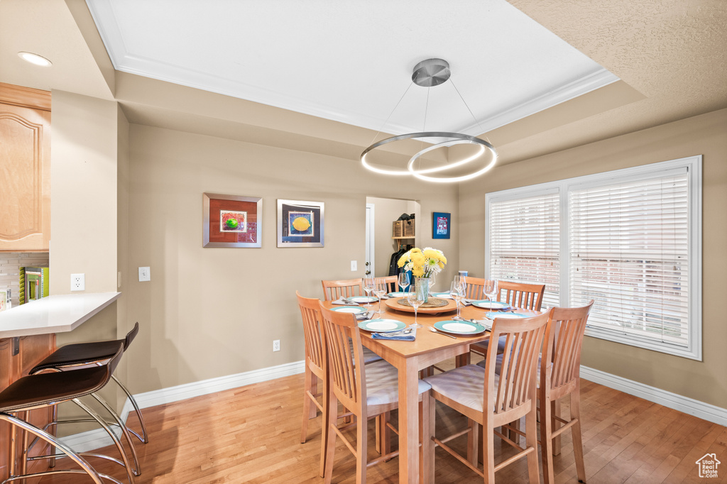 Dining room with light wood-style flooring, crown molding, a raised ceiling, and recessed lighting