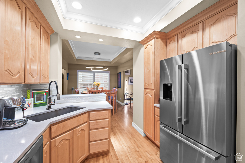 Kitchen with stainless steel refrigerator with ice dispenser, a raised ceiling, light wood-style floors, ornamental molding, and light countertops