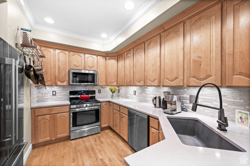 Kitchen featuring stainless steel appliances, light wood-style flooring, light countertops, ornamental molding, and backsplash