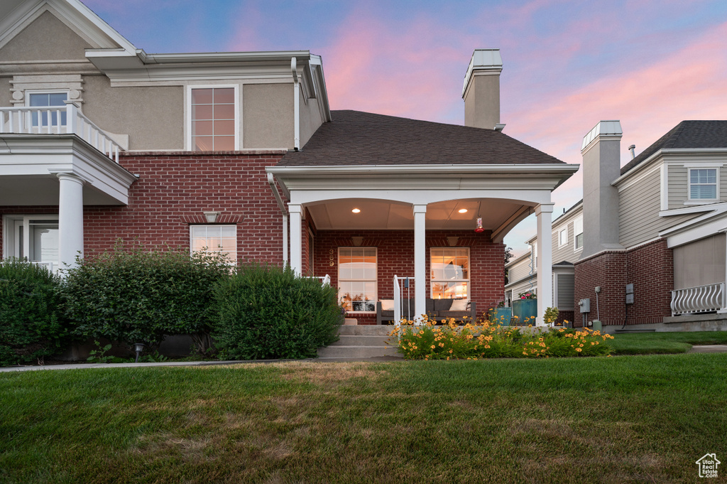 View of front of property with brick siding, a yard, and a porch