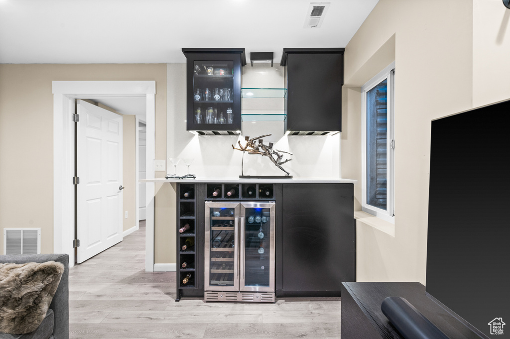 Indoor bar with beverage cooler and light wood-type flooring