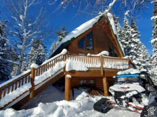 View of snowy exterior featuring a wooden deck and log exterior