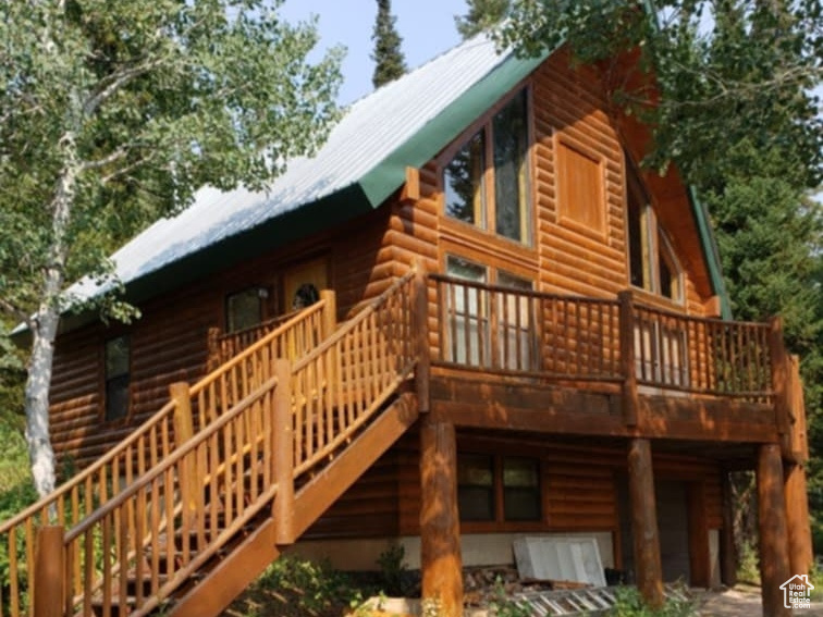 Back of property featuring log veneer siding, a deck, a garage, and a metal roof