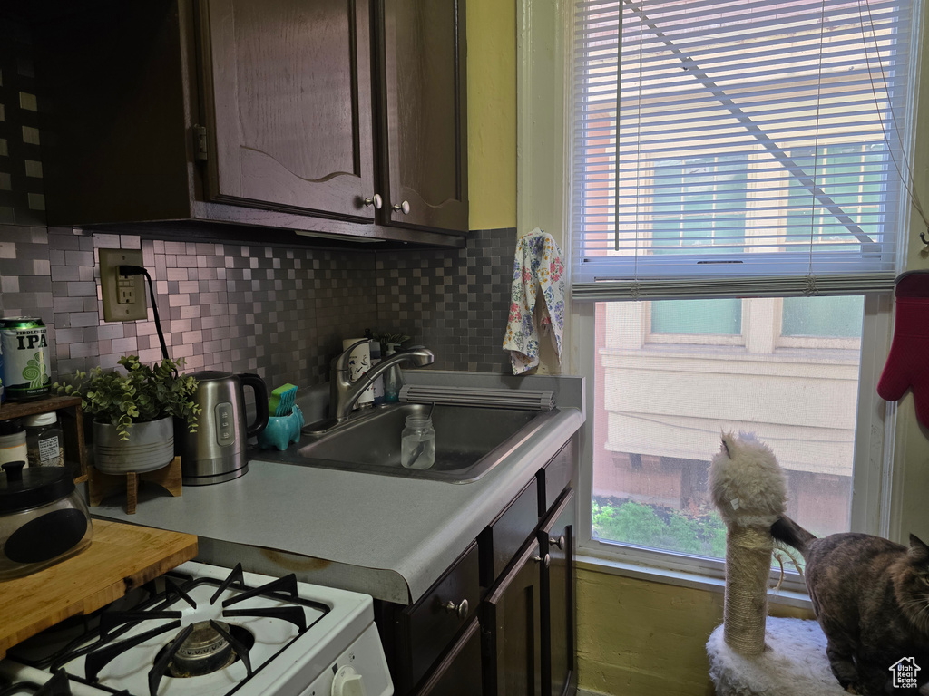 Kitchen featuring a sink, white gas stove, decorative backsplash, dark brown cabinets, and light countertops