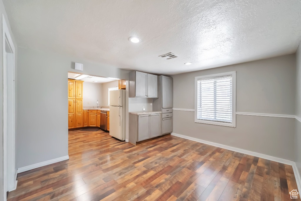 Kitchen with freestanding refrigerator, light countertops, a textured ceiling, dishwasher, and wood finished floors