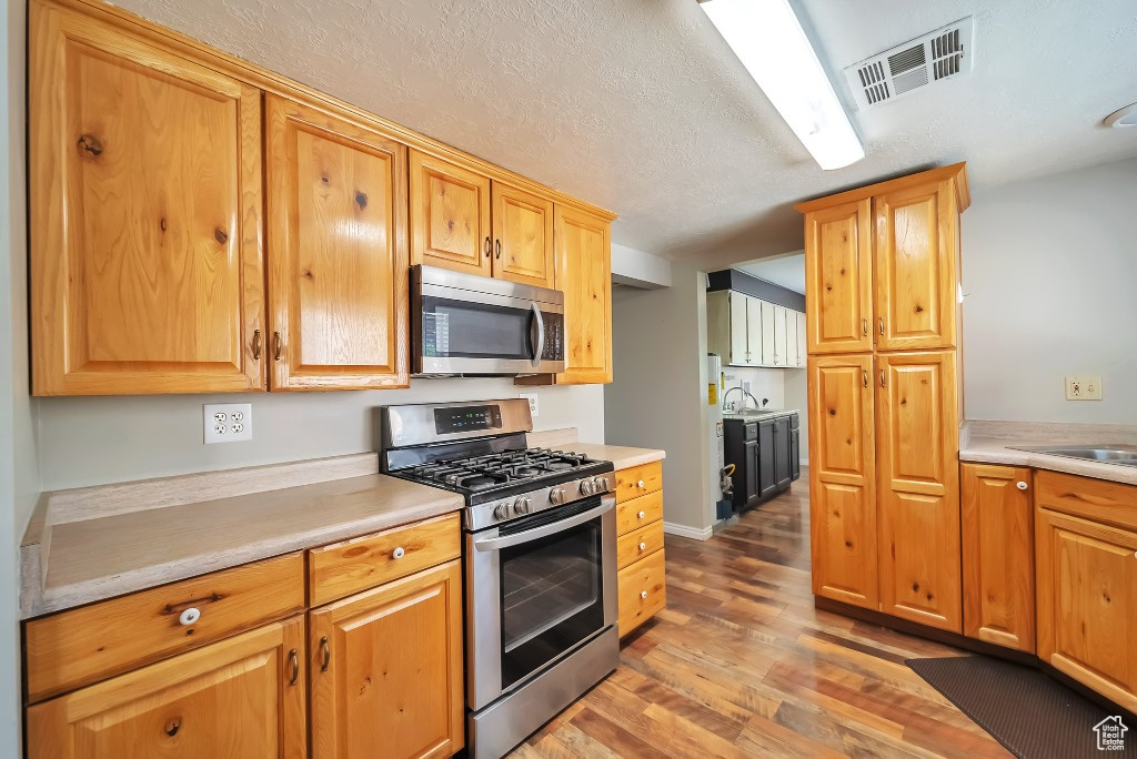 Kitchen with stainless steel appliances, light wood finished floors, light countertops, and a textured ceiling