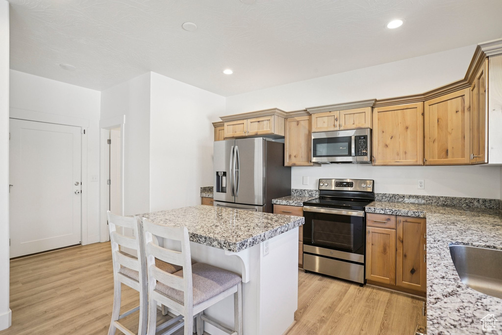 Kitchen featuring stainless steel appliances, light wood-style flooring, a kitchen bar, a kitchen island, and recessed lighting
