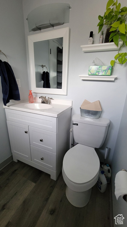Half bathroom with wood finished floors, toilet, and vanity