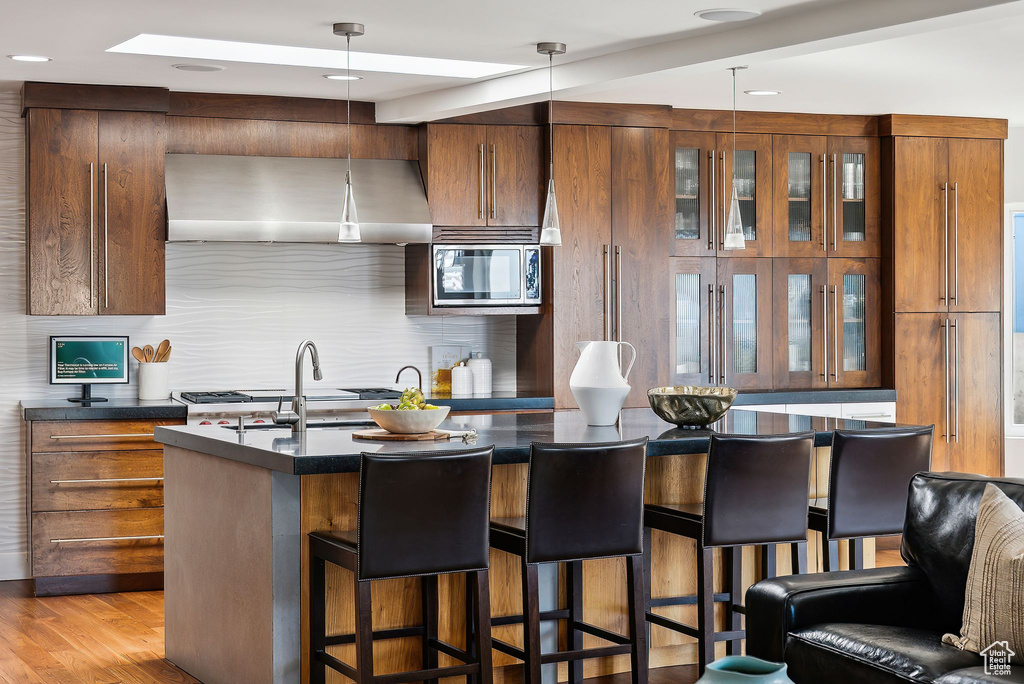 Kitchen with range hood, dark countertops, stainless steel microwave, a kitchen bar, and tasteful backsplash