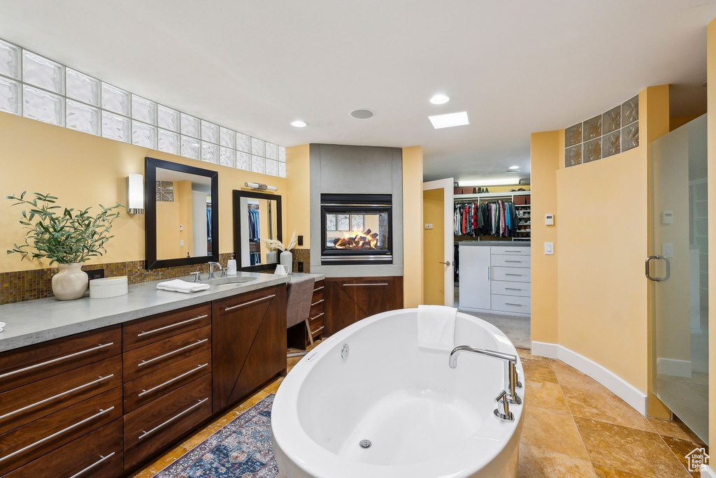 Bathroom with a spacious closet, vanity, a freestanding tub, a multi sided fireplace, and a shower stall