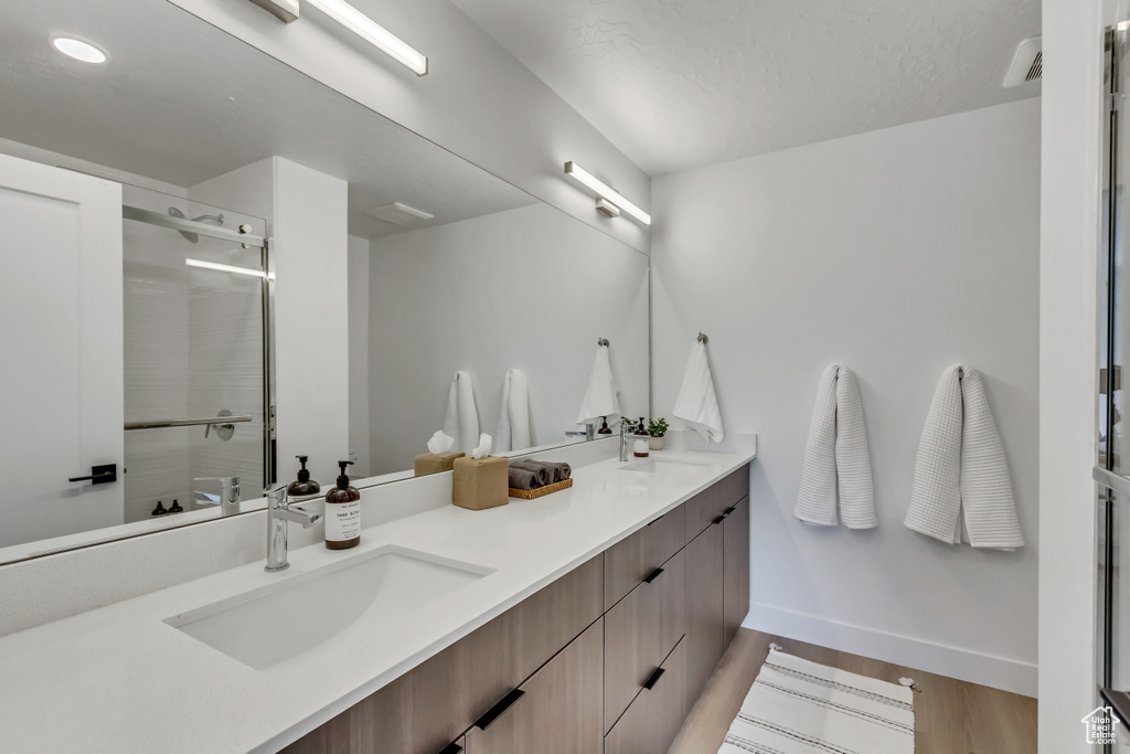 Bathroom featuring double vanity, a tile shower, and wood finished floors
