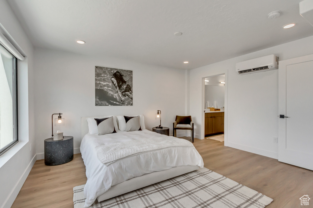 Bedroom featuring a wall unit AC, light wood-type flooring, recessed lighting, and ensuite bathroom