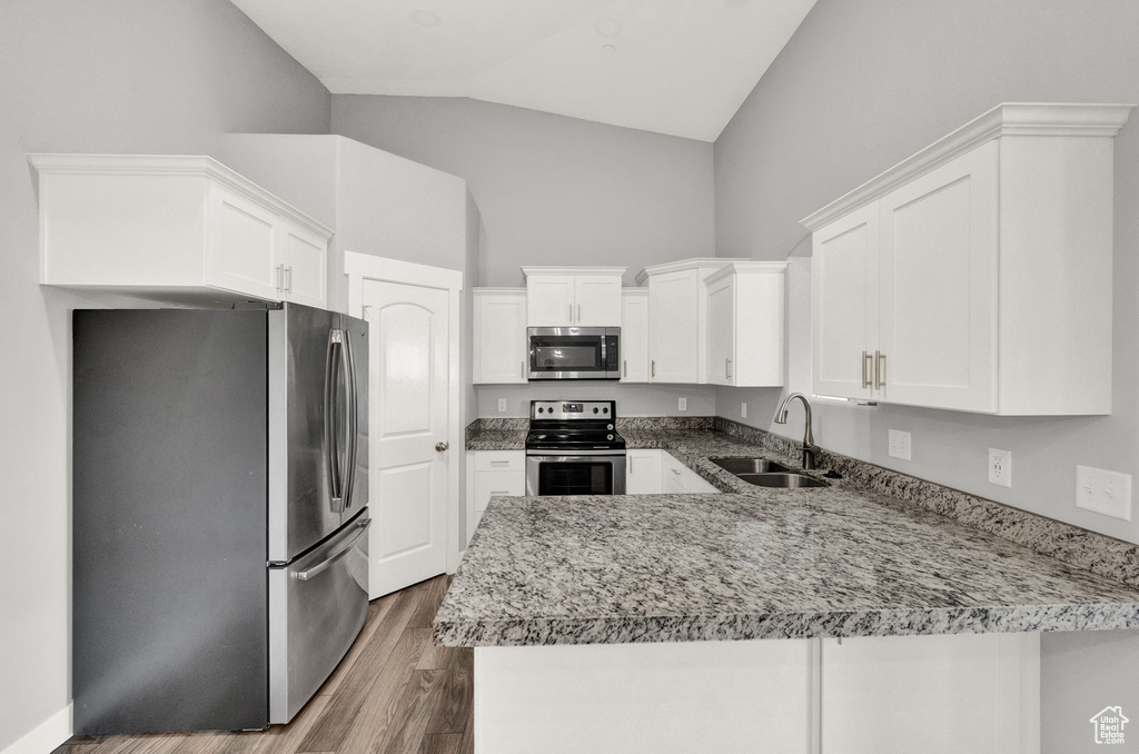 Kitchen featuring appliances with stainless steel finishes, a peninsula, wood finished floors, white cabinetry, and high vaulted ceiling