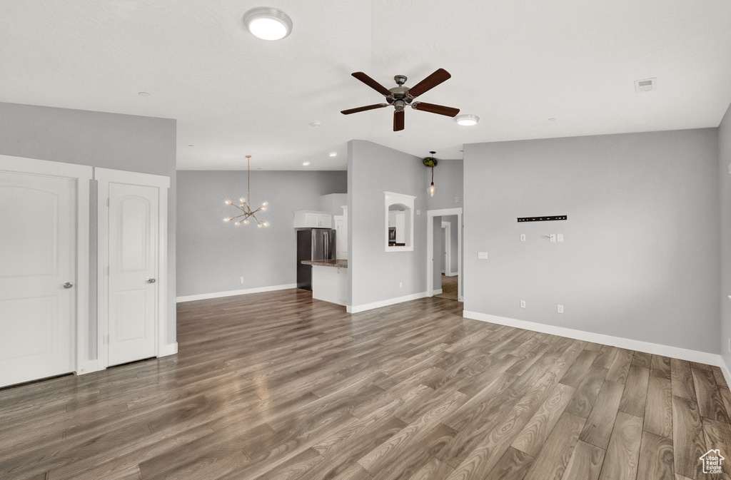 Unfurnished living room featuring a chandelier, ceiling fan, wood finished floors, and vaulted ceiling