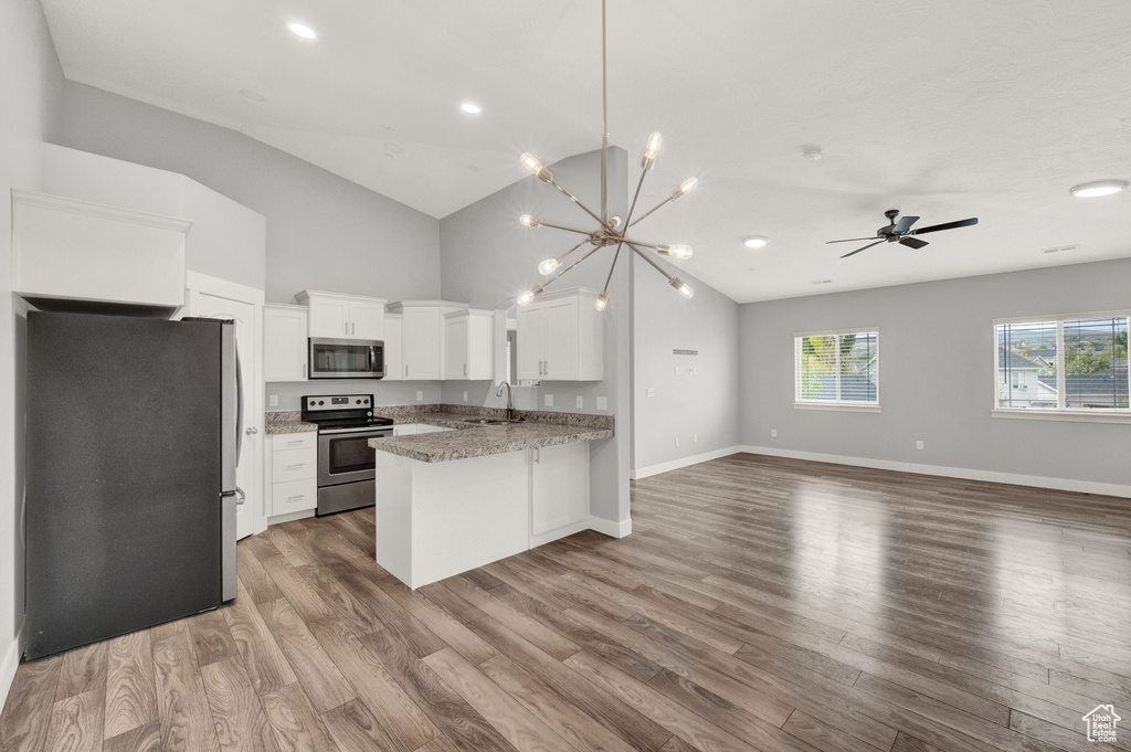 Kitchen with stainless steel appliances, open floor plan, a peninsula, white cabinets, and wood finished floors