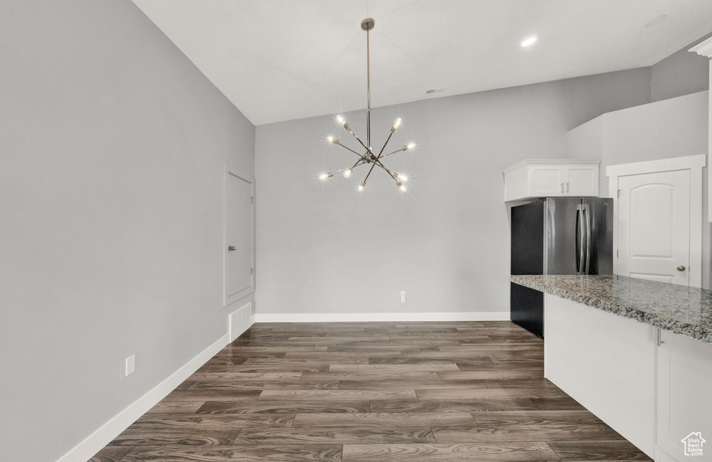 Unfurnished dining area with high vaulted ceiling, a chandelier, and dark wood-type flooring