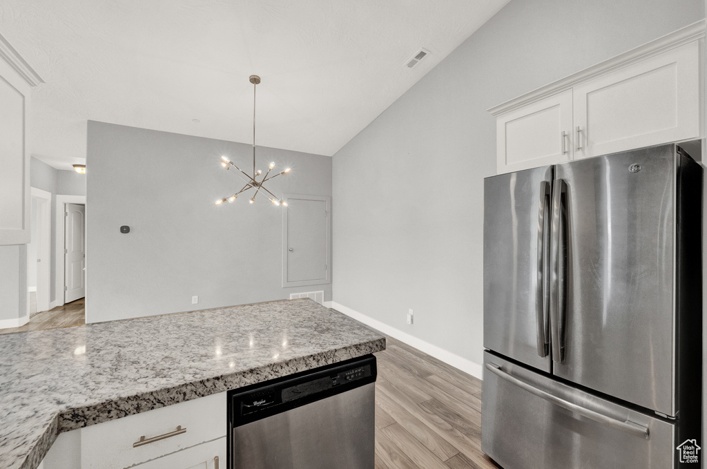 Kitchen featuring appliances with stainless steel finishes, light wood-type flooring, white cabinetry, vaulted ceiling, and a chandelier
