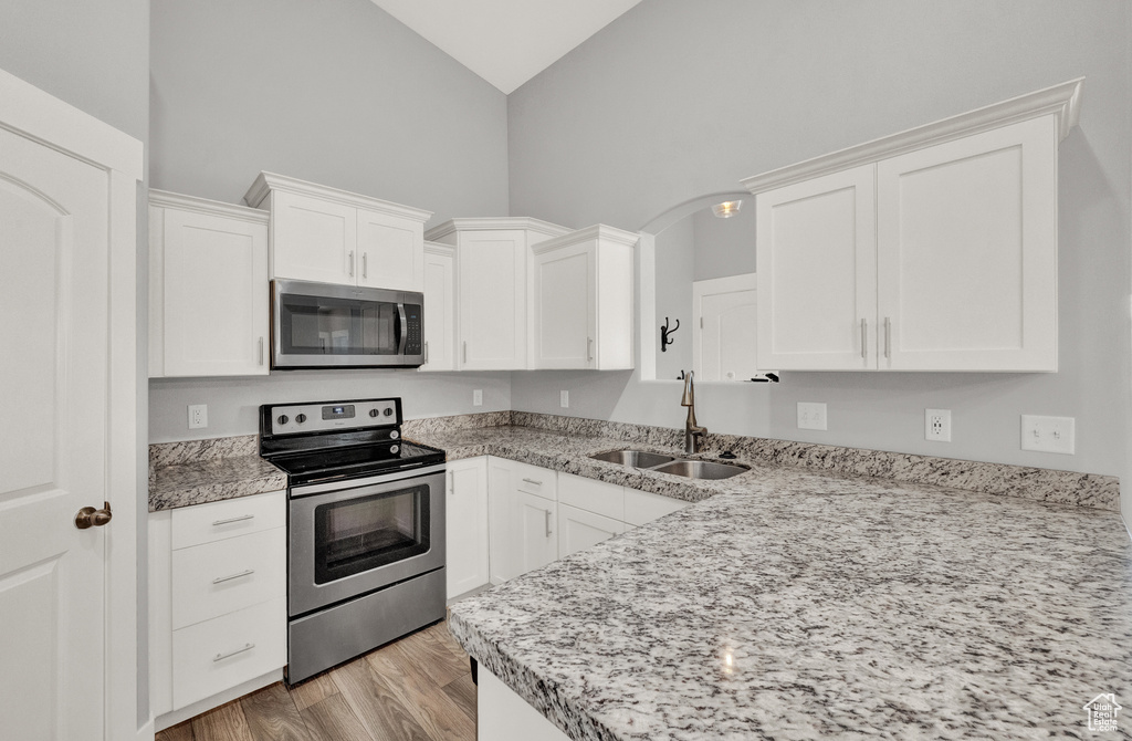 Kitchen featuring appliances with stainless steel finishes, high vaulted ceiling, white cabinetry, light wood-type flooring, and light stone counters