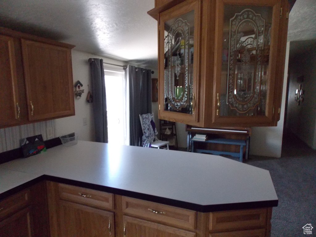Kitchen featuring a peninsula, carpet flooring, light countertops, and glass insert cabinets