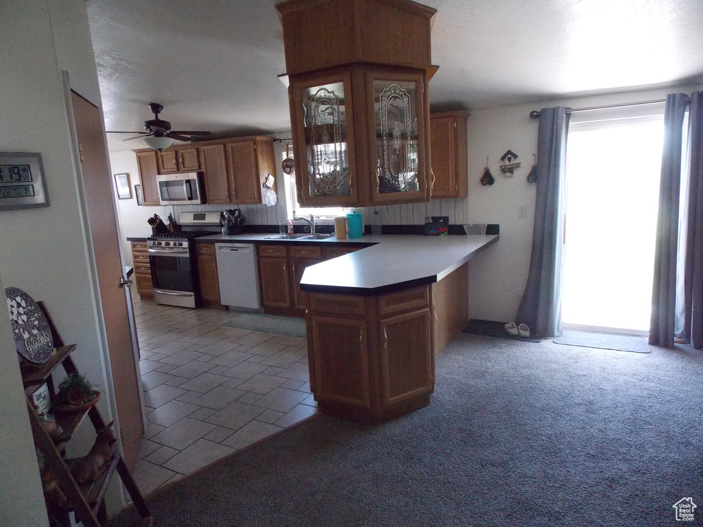 Kitchen with appliances with stainless steel finishes, ceiling fan, a peninsula, glass insert cabinets, and brown cabinets