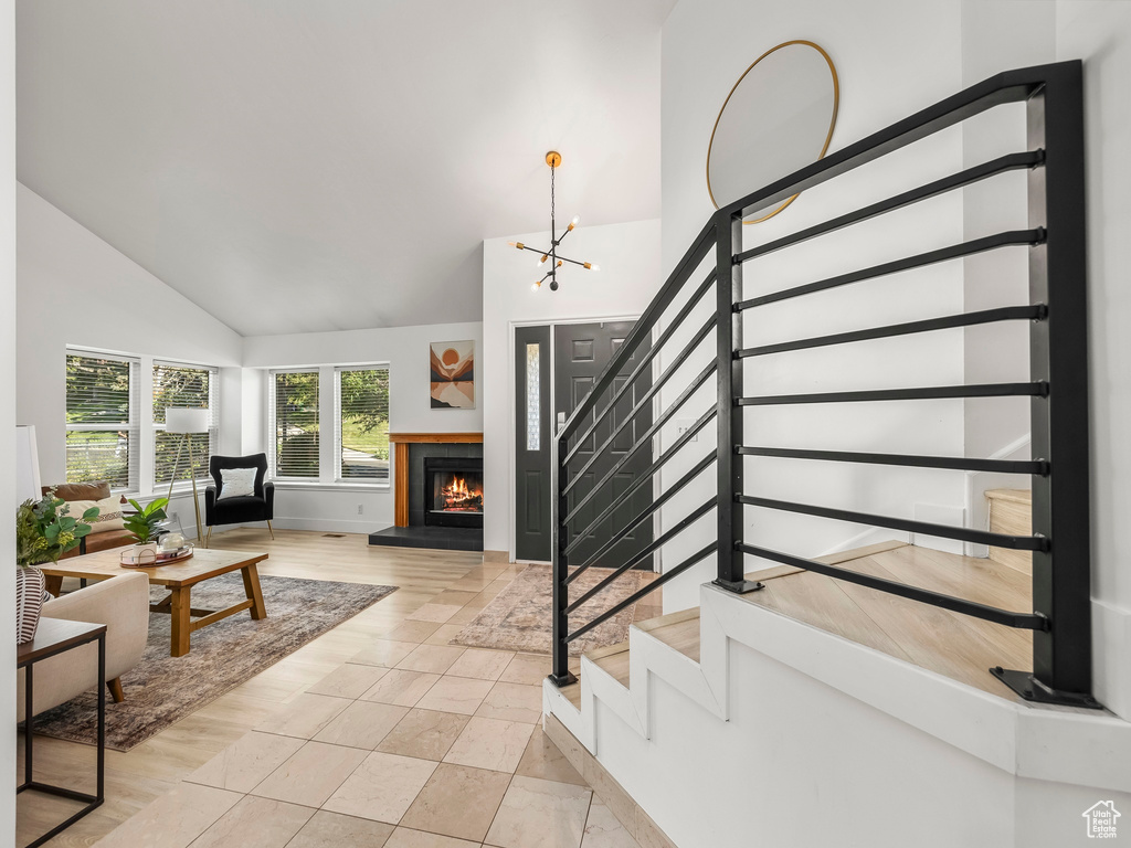 Living area featuring stairs, high vaulted ceiling, a warm lit fireplace, and a chandelier