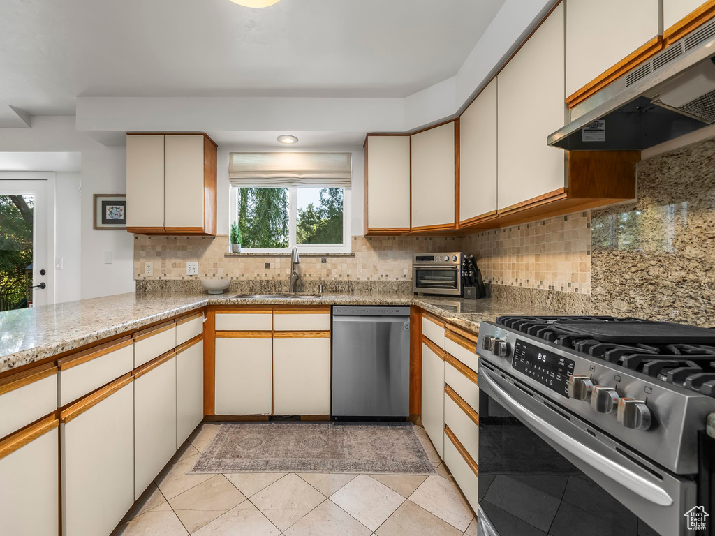 Kitchen with stainless steel appliances, under cabinet range hood, decorative backsplash, and plenty of natural light