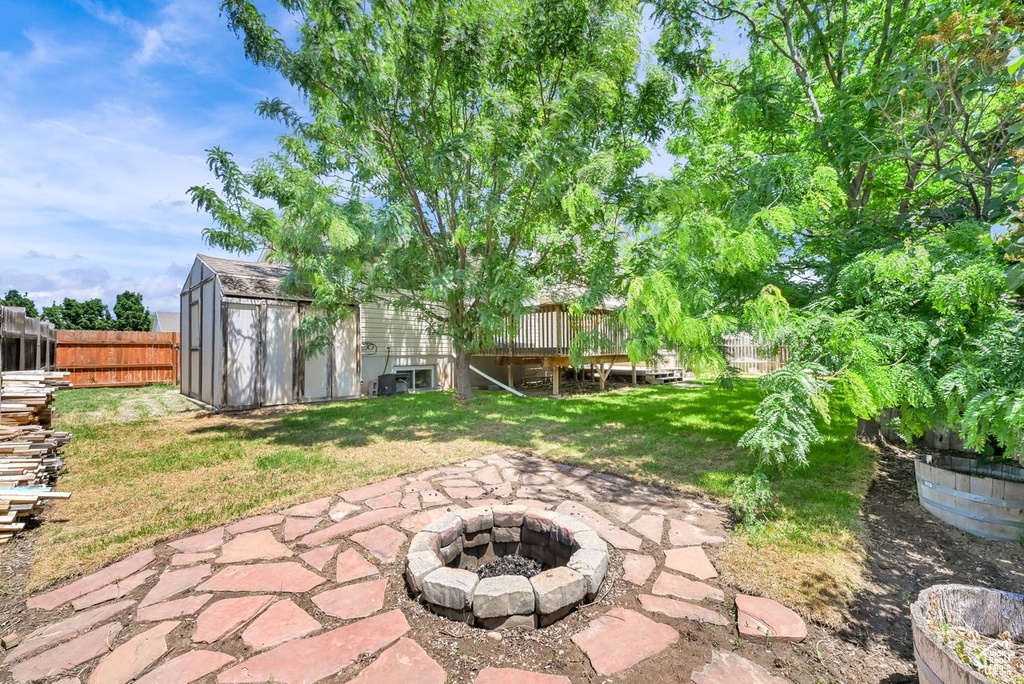 Fenced backyard with an outdoor fire pit, a storage unit, a deck, and a patio area