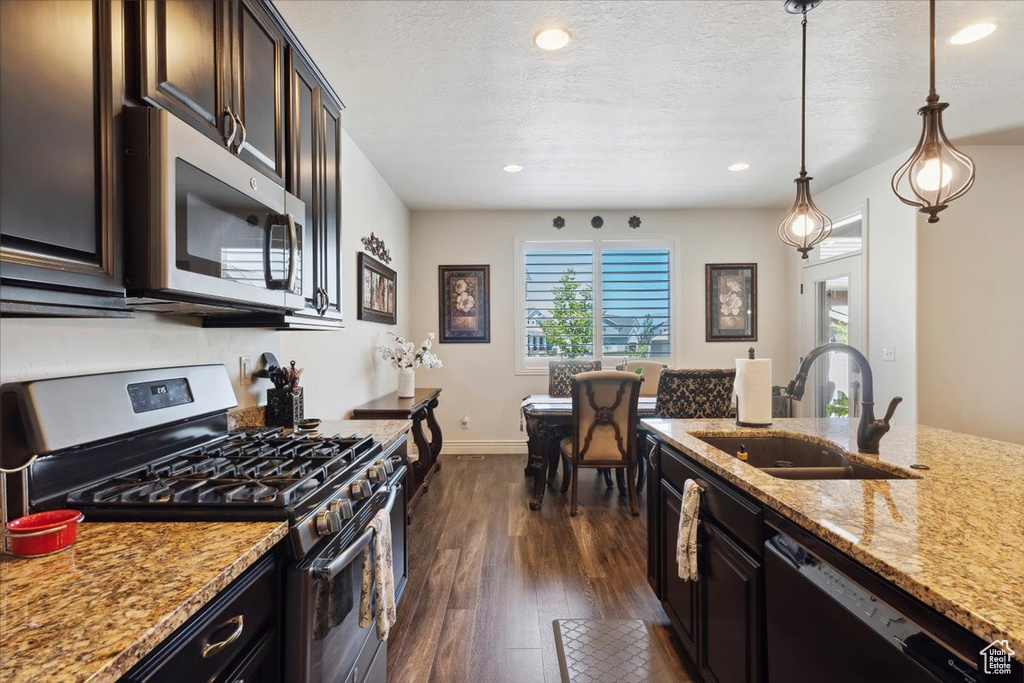 Kitchen with stainless steel appliances, dark wood-style floors, light stone countertops, recessed lighting, and decorative light fixtures