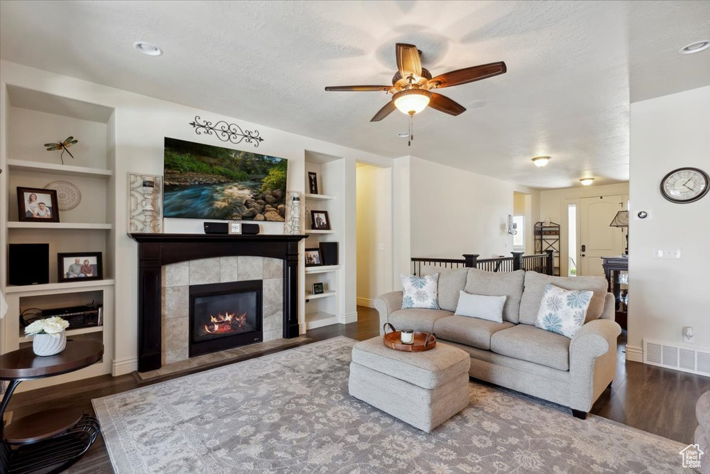 Living area with a tiled fireplace, built in features, wood finished floors, a ceiling fan, and a textured ceiling