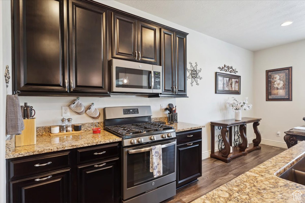 Kitchen with stainless steel appliances, dark wood-style flooring, light stone countertops, and recessed lighting