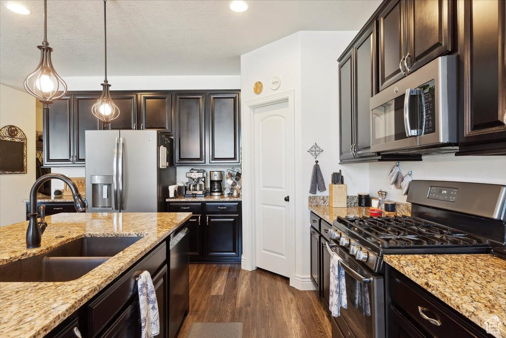 Kitchen with appliances with stainless steel finishes, light stone countertops, dark wood finished floors, hanging light fixtures, and recessed lighting
