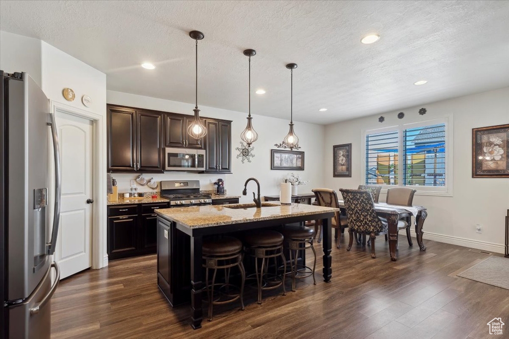 Kitchen featuring appliances with stainless steel finishes, a kitchen breakfast bar, dark wood-style flooring, light stone countertops, and recessed lighting
