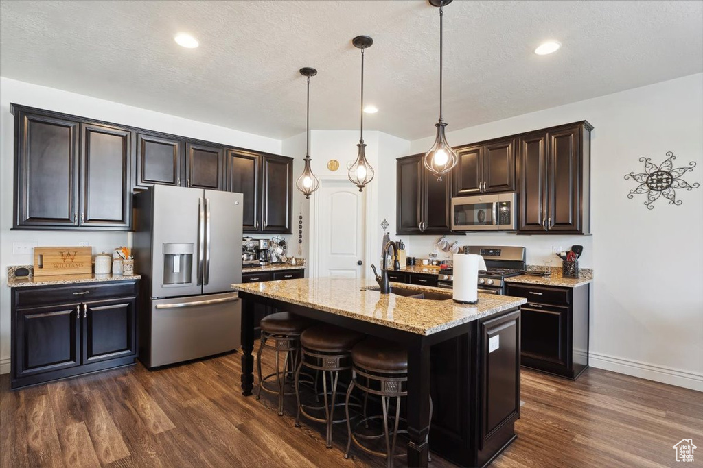 Kitchen featuring appliances with stainless steel finishes, dark wood-type flooring, light stone counters, a kitchen breakfast bar, and hanging light fixtures